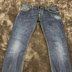 Blå jeans från Dondup - Säljer ett par snygga blå jeans från Dondup. De har en klassisk femficksdesign med gul kontrastsöm som ger en cool look. Jeansen är i bra skick och har en knappgylf. Perfekta för vardagsbruk eller en avslappnad utekväll!