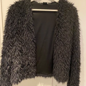 Svart pälsjacka från Gina Tricot - Säljer en supermjuk och fluffig svart pälsjacka från Gina Tricot. Perfekt för att hålla sig varm och stilren under kyliga dagar. Jackan har långa ärmar och en öppen design utan knappar eller dragkedja. Den är i storlek S och passar perfekt för både vardag och festliga tillfällen.
