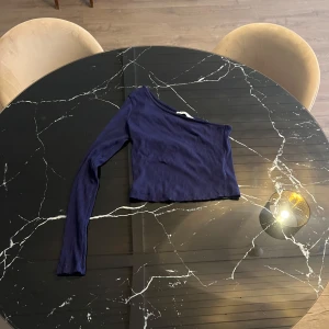 Mörkblå oneshoulder topp från NA-KD - Snygg mörkblå oneshoulder topp från NA-KD i ribbat material. Perfekt för en trendig look med sin unika design och långa ärm. Passar utmärkt till både jeans och kjol.