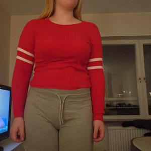 Röd ribbad tröja med vita ränder - Snygg röd ribbad tröja med vita ränder på ärmarna. Tröjan har en tight passform och långa ärmar, perfekt för en sportig look.