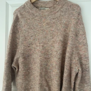 Beige stickad tröja från Carin Wester - Mysig beige stickad tröja från Carin Wester i storlek S. Tröjan har en melerad design med inslag av rosa och grått, samt långa ärmar och ribbade muddar. Perfekt för kyliga dagar!