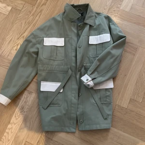 Grön jacka från Missguided - Snygg grön jacka från Missguided med vita detaljer och flera praktiska fickor. Jackan har en klassisk krage och knäppning framtill. Perfekt nu till våren. Jackan är som ny för den är knappt använd🫶