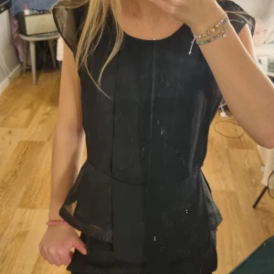 Svart blus - Elegant osymmetrisk svart topp från Size & Needle med transparenta detaljer. Toppen har en rund hals och är ärmlös med en öppen rygg. Har köpt secondhand men aldrig riktigt kommit till andvänding, använt ca 1/2 gånger💕
