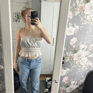 Vit satinlinne med smala axelband - Säljer ett stilrent vitt satinlinne med smala axelband och elastisk midja. Toppen har en lätt glansig yta och är perfekt för en somrig look. Passar bra till jeans eller kjol. 