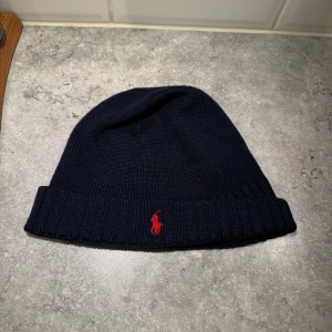 Mörkblå mössa från Polo Ralph Lauren - Snygg mörkblå mössa från Polo Ralph Lauren med röd broderad logotyp framtill.|| mössan är den nyskick och använd ett fåtal gånger|| säljer den mössan för endast 300kr|| tveka inte att höra av er vid frågor eller funderingar mvh Linus