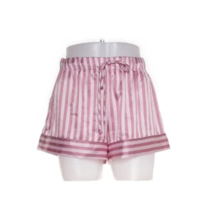 Rosa randiga silkiga pjamas shorts, Victoria's Secret - Silkiga rosa och vita randiga pjamas shorts från Victoria's Secret. De har en bekväm passform med knytband i midjan och är perfekta för en avslappnad stil. Tillverkade i ett mjukt och glansigt material.