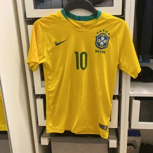 Brasilien fotbollströja från Nike - Säljer en gul Brasilien fotbollströja från Nike med nummer 10 och Neymar Jr på ryggen . Perfekt för fotbollsfans som vill visa sitt stöd för Brasilien! Tröjan är i ett helt okej skick och i storlek XS.