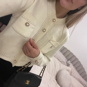 Beige cardigan med pärlknappar - En elegant beige/cremevit cardigan med dekorativa pärlknappar och två bröstfickor. St S