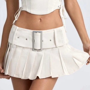 Vit kortkjol med bälte - Trendig vit kortkjol med ett brett bälte och plisserad design. Kjolen har en stilren look och passar perfekt för en modern outfit. Nypris 760kr. Ny med lappar kvar.