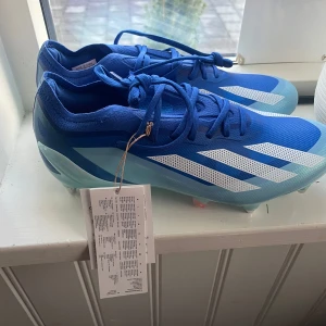 Adidas X Crazyfast.1 SG fotbollsskor - Snygga blå Adidas X Crazyfast.1 SG fotbollsskor med vita detaljer och snörning. Skorna har en lätt och smidig design med metallskruvdobbar. Helt oanvända!!💙🩵 kan tänka mig att gå ner i pris vid snabb affär.