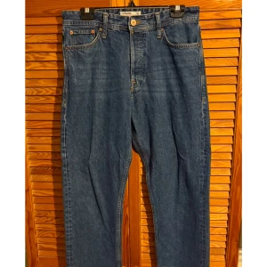 Blå jeans från Jack & Jones - Säljer ett par klassiska blå jeans från Jack & Jones. De har en rak passform med fem fickor och knappgylf. Perfekta för en avslappnad stil.