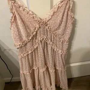 Ljusrosa klänning från NA-KD - Söt ljusrosa klänning från NA-KD med volangdetaljer och ett diskret blommönster. Klänningen har en v-ringad design och är ärmlös, perfekt för varmare dagar. Klänningen har använts fåtal gånger och passar perfekt till midsommar. Passar bra till mig som har S/36 i storlek.