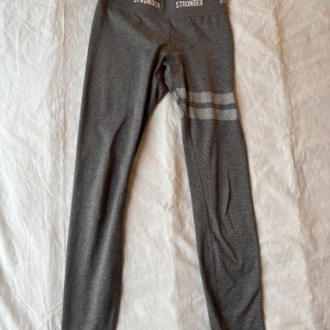 Gråa tränings tights från Stronger - Snygga grå tränings tights från Stronger med vita prickiga detaljer runt låren. Perfekta för träning eller en avslappnad dag. De är stretchiga och bekväma med en tight passform. Säljer för att den är försmå och för korta för mig som är 1,74cm. Skulle även passa xs💕