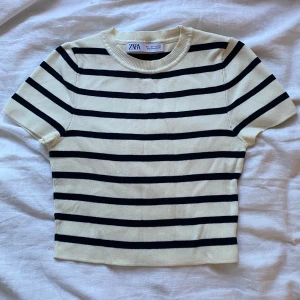 Randig kortärmad topp från Zara - Snygg kortärmad topp från Zara i beige och svart med klassiskt randigt mönster. Perfekt för en stilren look.