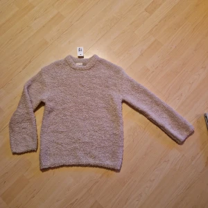 Beige fluffig tröja från Kappahl storlek 158/164. Passar även XS - Mysig beige tröja från Kappahl i en fluffig och mjuk polyesterblandning. Perfekt för kyliga dagar med sin långärmade design och bekväma passform. Ett måste för garderoben! Helt ny med prislappen kvar.