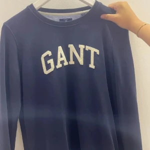 Mörkblå sweatshirt från GANT - Snygg mörkblå sweatshirt från GANT med vit logotyp på bröstet. Tröjan har långa ärmar och en klassisk rund halsringning. Perfekt för en avslappnad stil.