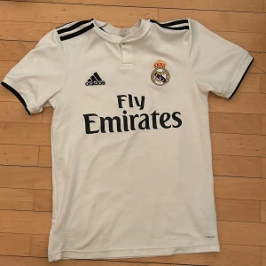 Vit Real Madrid fotbollströja från Adidas - Säljer en vit Real Madrid fotbollströja från Adidas. Tröjan är ganska sliten då den är från 2018. Säljer den eftersom den är för liten för mig. 