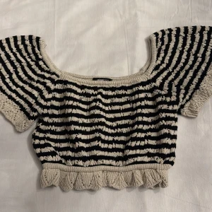 Randig stickad topp - Säljer en unik stickad topp med svartvita ränder och volangdetalj vid nederkanten. Toppen har korta ärmar och en fyrkantig halsringning. Perfekt för en trendig look!