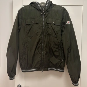 Mörkgrön Moncler vindjacka - Pris kan diskuteras!                                             Snygg grön vindjacka från Moncler, även kallad  Jeanclaude Giubbotto Jeanclaude jacket.                 Den är i toppskick utan några flaws och nästan oanvänd.                                                               Storleken är 3 vilket passar perfekt för S/M. Jackan är perfekt för både hösten och våren!