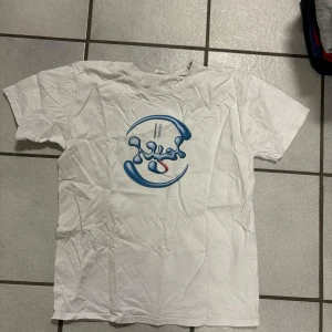 Vit t-shirt med blått tryck - Säljer en vit t-shirt med ett unikt blått tryck på framsidan. T-shirten har korta ärmar och är i en normal passform. Perfekt för en avslappnad stil. Velo ice cool 