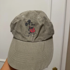 Grön keps med mickey mouse - Kepsen har en klassisk design med justerbar rem baktill för perfekt passform. Aldrig använt. 