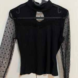 Svart topp med meshärmar - Snygg svart topp med transparenta meshärmar och prickigt mönster. Toppen har en hög hals..