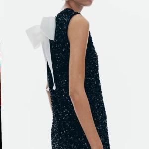 Gullig svart glittrig klänning med rosett - Supersöt svart klänning med glittrigt mönster och en stor vit rosett i ryggen. Ärmlös design som ger en stilren look🥰🥰 helt oanvänd med lappen kvar. Nypris 399 helt slutsåld!