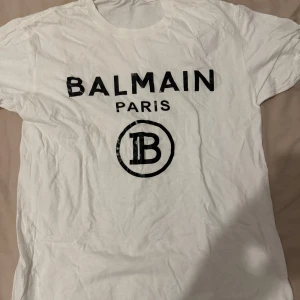Vit och svart t-shirt från Balmain - Snygga t-shirts från Balmain i både vit och svart med det ikoniska Balmain Paris-trycket på framsidan. Perfekt för en stilren och modern look. Går att köpa separat också