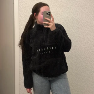 Svart fleece hoodie från Dope - Mysig svart fleece hoodie från Dope med halv dragkedja och broderad text på framsidan. Perfekt för kyliga dagar med sin fluffiga och varma design. Den har en avslappnad passform och är idealisk för både inomhus och utomhus.