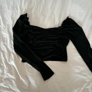 Svart topp - Snygg svart topp med långa ärmar och rynkade detaljer. Perfekt för en elegant look.