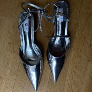 Silvriga pumps med spetsig tå - Snygga silvriga pumps med spetsig tå och smal klack. Skorna har en elegant remdesign som ger extra stil. Perfekta för att lyfta din outfit till nästa nivå.