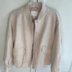 Beige vårjacka från H&M - Snygg beige vår/bomberjacka från H&M med knappar framtill. Jackan är helt oanvänd och i linnematerial. Köparen står för frakten!