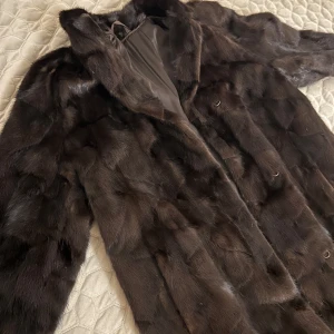 Äkta designer Minkpäls jacka   - Säljer en elegant mörkbrun pälsjacka med lång ärm och klassisk design. Jackan har en mjuk och lyxig känsla, perfekt för kalla dagar. Den är lång och täcker bra, vilket ger extra värme och stil. Från märket Dosca. Äkta mink päls. 