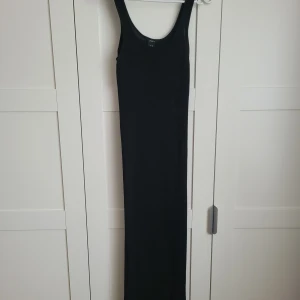 Svart långklänning från Lindex - Elegant svart långklänning från Lindex i ett ribbat material. Klänningen är ärmlös och har en stilren design som passar perfekt för olika tillfällen. Den är tillverkad i ett mjukt och bekvämt tyg som ger en smickrande passform.