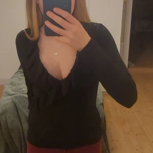 Svart långärmad topp med volangdetaljer - Snygg svart långärmad topp med volangdetaljer vid halsringningen. Perfekt för en stilren look. Passar bra till både jeans och kjol. Tröjan är i storlek M menpassar jätte bra på mig som är s/xs💞