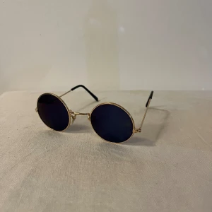 Solglasögon  - Runda mindre solglasögon. Mörkblå nästan svart glas och guldig ram
