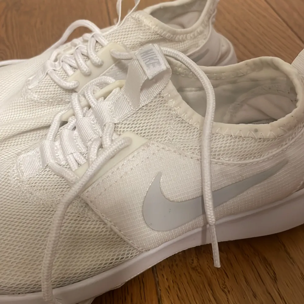 Säljer ett par vita Nike sneakers i nyskick. De har en stilren design med snörning och en bekväm passform. Perfekta för både träning och vardagsbruk. Sulan är i bra skick och de är väldigt lätta att matcha med olika outfits.. Skor.