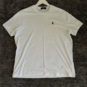 Vit t-shirt från Ralph Lauren - Säljer en klassisk vit t-shirt från Ralph Lauren. Den har en liten broderad logga på bröstet och är gjord i mjuk bomull. Perfekt för en avslappnad stil. Passar till allt och är superbekväm! 