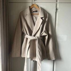 Beige kappa från Gina Tricot, Pris kan diskuteras  - Säljer en superfin beige kappa från Gina Tricot för 500kr i storlek XL. Den har en klassisk design med ett bälte i midjan för en snygg passform. Perfekt för höst och vår, och den är gjord i ett mjukt material som känns lyxigt. Kappan har långa ärmar och en stilren krage.