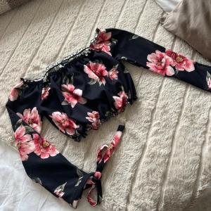 Off shoulder topp med snörning i ärmarna - Off shoulder topp från new look. Snörning i ärmarna. Svart med söta blommor. Använd sparsamt. Storlek S