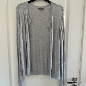 Grå kofta från Basic You - Säljer en stilren och bekväm grå kofta från Basic You. Den är i storlek S och har långa ärmar. Perfekt för lager-på-lager under höst och vår. Koftan har knappar framtill och är i ett mjukt material som känns skönt mot huden.