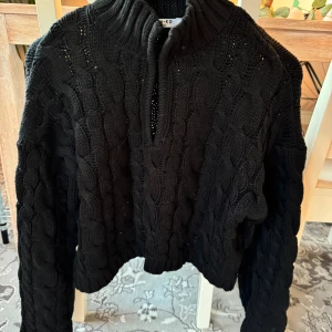 Svart stickad tröja från NA-KD - Säljer en supermysig svart stickad tröja från NA-KD. Den har ett snyggt flätmönster och en djup v-ringning som ger en cool look. Perfekt för höst och vinter när du vill hålla dig varm och stilren. Tröjan är i storlek S och är i nyskick. Perfekt för både vardag och fest!