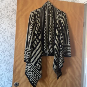 Mönstrad cardigan från Chesley - Säljer en superfin mönstrad cardigan från Chesley i storlek M. Den har ett coolt geometriskt mönster i svart och beige, perfekt för att liva upp vilken outfit som helst. Den är långärmad och har en avslappnad passform som gör den både bekväm och stilren. Perfekt för höst och vår!