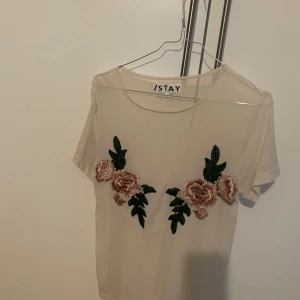 Beige topp med blommigt broderi från ISTAY - Säljer en superfin beige topp från ISTAY med vackert blommigt broderi i rosa och grönt framtill. Toppen är kortärmad och perfekt för en somrig look. Den är i nyskick och redo för nya äventyr! den är genomskinlig.