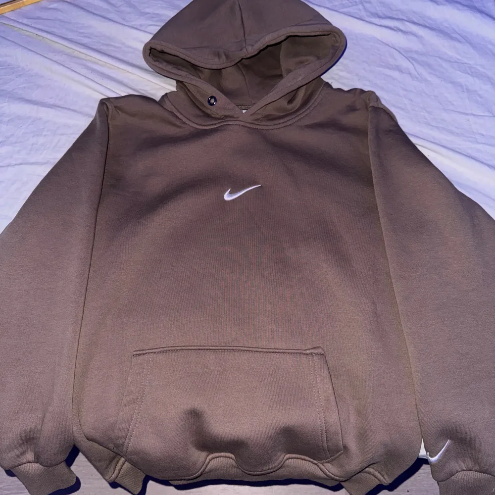 Säljer en snygg brun hoodie från Nike i storlek S. Den har en klassisk design med en liten vit Nike-logga på bröstet och ärmen. Hoodien är perfekt för höst och vinter med sin mysiga känsla och ribbade muddar vid ärmsluten. Perfekt för både träning och vardag!. Hoodies.