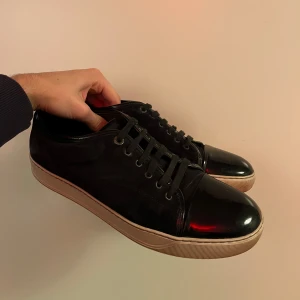 Svarta sneakers från Lanvin - Säljer ett par stilrena svarta sneakers från Lanvin. De har en glansig tå och snörning framtill. De är i bra skick och är i storlek 44. Mvh Charlie