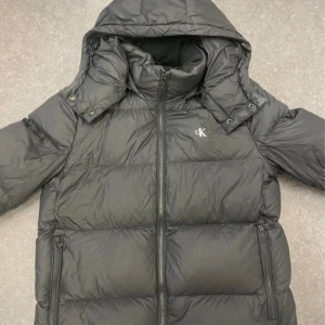 Svart dunjacka från Calvin Klein - Säljer en snygg svart dunjacka från Calvin Klein i storlek M men ja skulle säga att den sitter mer som en S🤗. Har ett litet hål i ena armen men annars inga defekter💕 Nypris 2,699kr