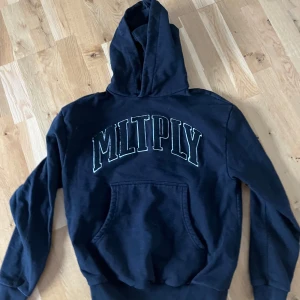 Svart hoodie från Multiply Apparel - Säljer en svart hoodie från Multiply Apparel i storlek XS. Den har en stor ficka fram och texten 'MLTPLY' i vitt på ryggen. Perfekt för en avslappnad stil eller kyliga dagar. 🖤