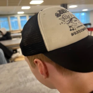 Svart och vit keps med tryck - Hej, säljer nu min vän elliot med kepsen på köpet