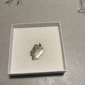 Guldigt hängsmycke med profilmotiv - Säljer ett unikt guldigt hängsmycke med ett detaljerat profilmotiv. Perfekt för att ge en personlig touch till ditt halsband eller armband. Smycket är i mycket bra skick och kommer i en stilren förpackning. Passar både till vardags och festliga tillfällen.